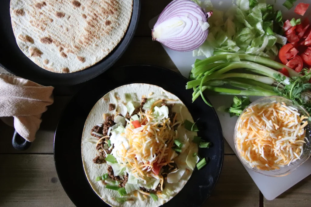 A close-up of restaurant-style smash burger tacos filled with crispy smashed beef patties, melted cheese, fresh lettuce, pickles, diced onions, and creamy burger sauce on toasted tortillas.