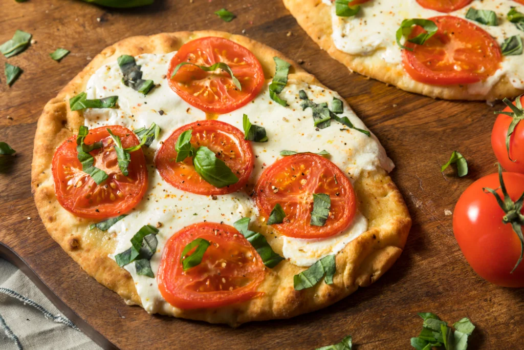 Freshly baked cottage cheese flatbread pizza topped with melted mozzarella, cherry tomatoes, basil leaves, and herbs, served on a wooden board for a healthy high-protein meal.