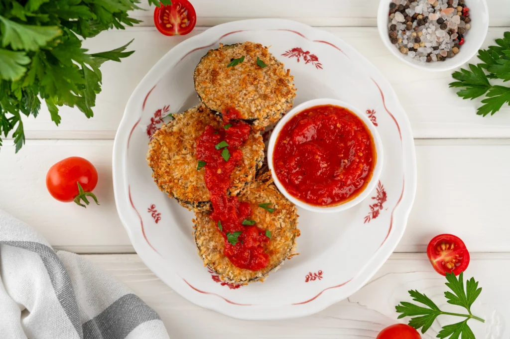 Crispy ground chicken Parmesan patties served with fresh parsley, grated Parmesan cheese, and marinara sauce on a white plate.
