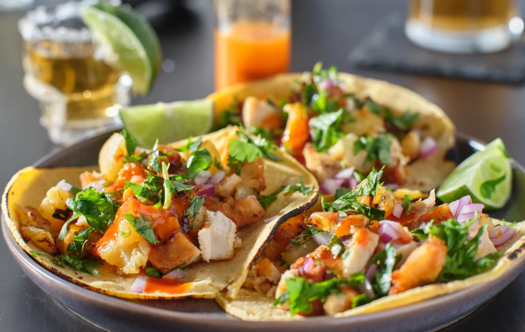 Fresh fish tacos served in warm corn tortillas with crispy white fish, shredded cabbage, avocado slices, pico de gallo, cilantro, lime wedges, and a creamy cilantro-lime sauce.