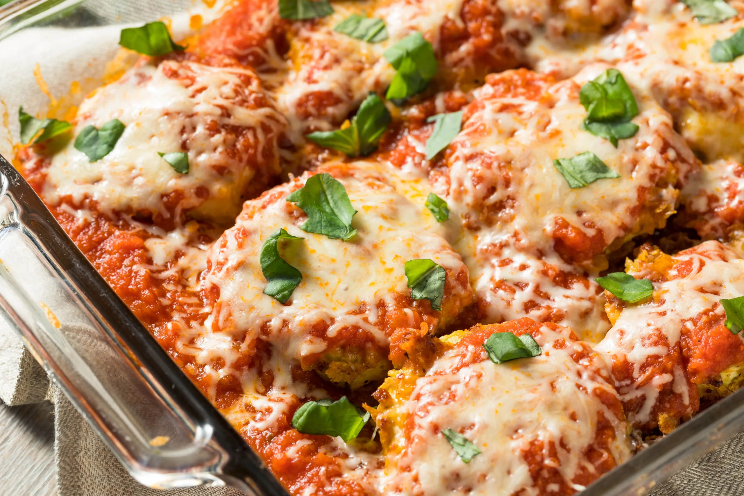 Crispy ground chicken Parmesan patties served with fresh parsley, grated Parmesan cheese, and marinara sauce on a white plate.