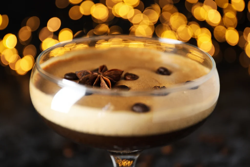 Classic Espresso Martini served in a chilled martini glass with a creamy foam topping and three coffee beans, set beside fresh espresso and coffee beans on a dark bar surface.