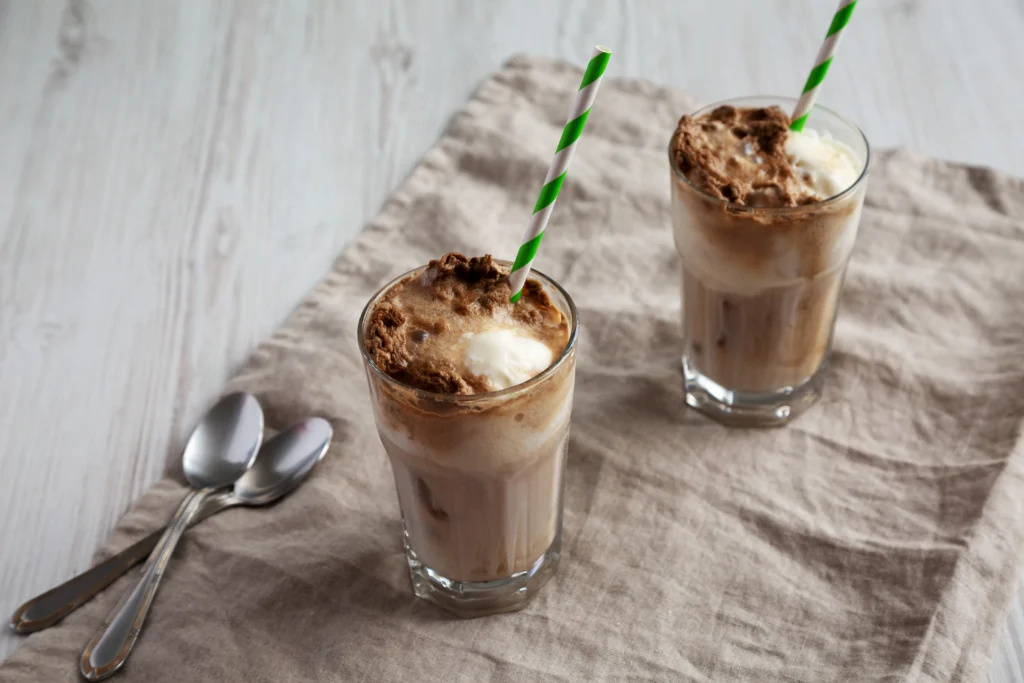 Refreshing homemade iced mochas served in clear glasses with chocolate drizzle, whipped cream, and ice cubes on a wooden table during summer.