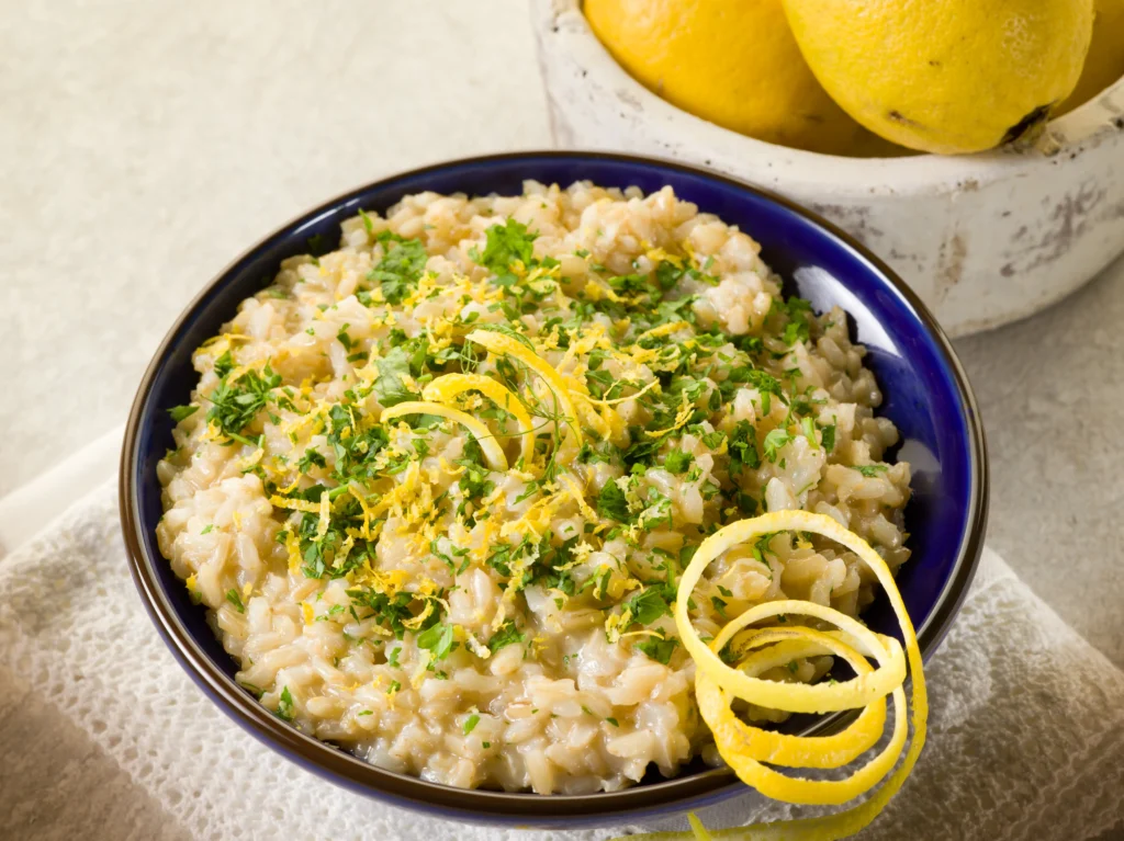 Creamy lemony risotto served with fresh Parmesan cheese, lemon zest, herbs, and cracked black pepper in a rustic white bowl.