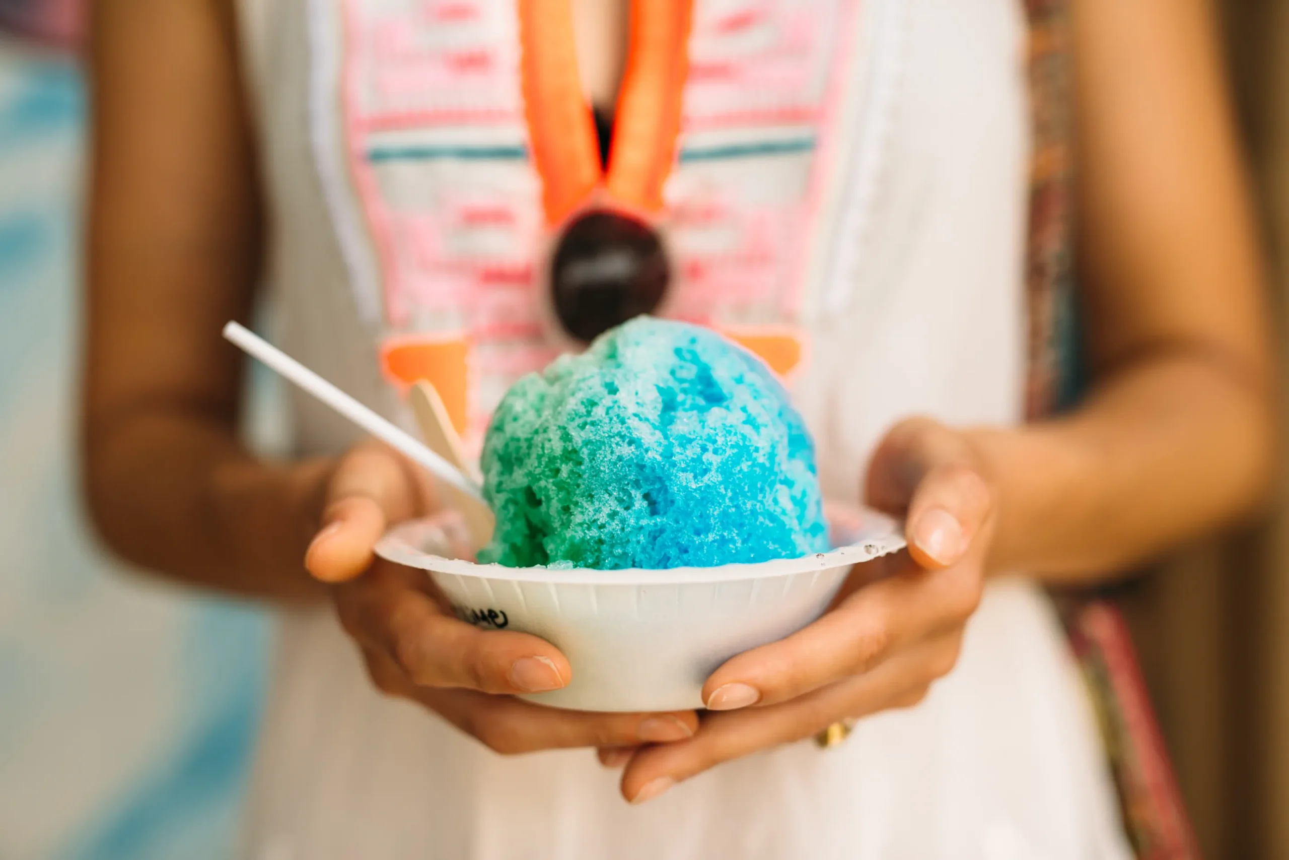 Homemade snow cone syrup in colorful bottles with shaved ice, fresh fruit, and summer toppings on a wooden table.