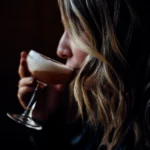 Classic Espresso Martini served in a chilled martini glass with a creamy foam topping and three coffee beans, set beside fresh espresso and coffee beans on a dark bar surface.