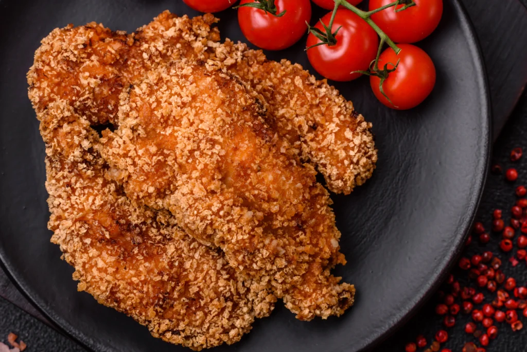 Golden baked cornflake chicken with a crispy golden coating, served on a plate with mashed potatoes, fresh green beans, and a sprinkle of parsley.